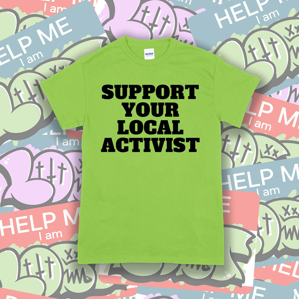 The original Support Your Local Activist t-shirt. Bold black letters screen printed on a lime green shirt. The shirt is displayed against a wall of colorful graffiti stickers.