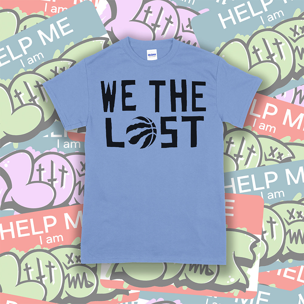 We The Lost t-shirt. Bold black lettering screen printed on a light blue shirt. Assorted colorful graffiti stickers make up the background.